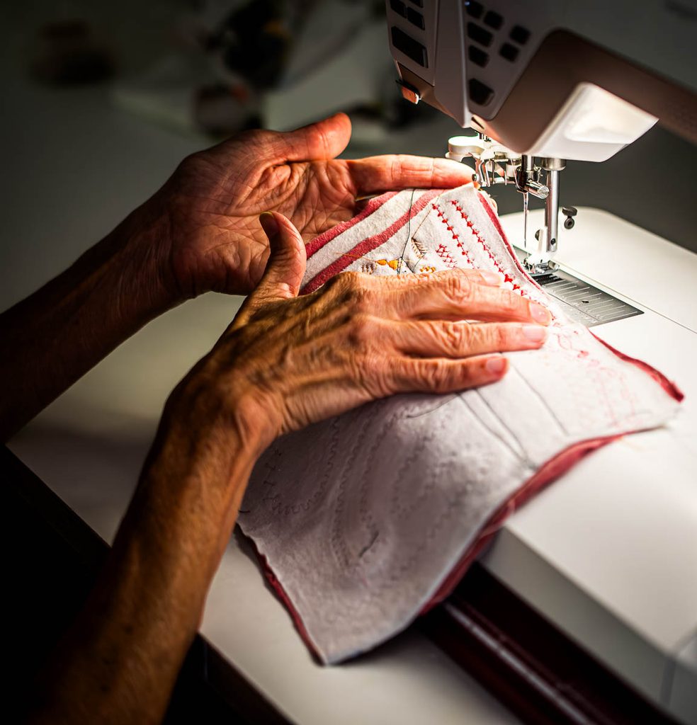 Image shows quilter's hands moving a block of fabric under a sewing machine's light.