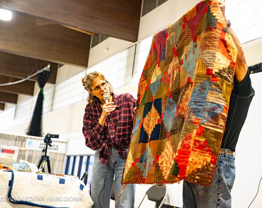Quilter Kristen Edens stands with a microphone next to a quilt.