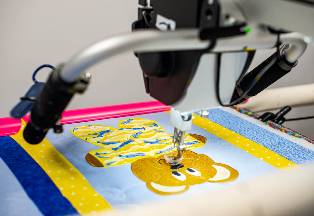 An emroidery machine stitches an image of a bear onto a block of fabric.
